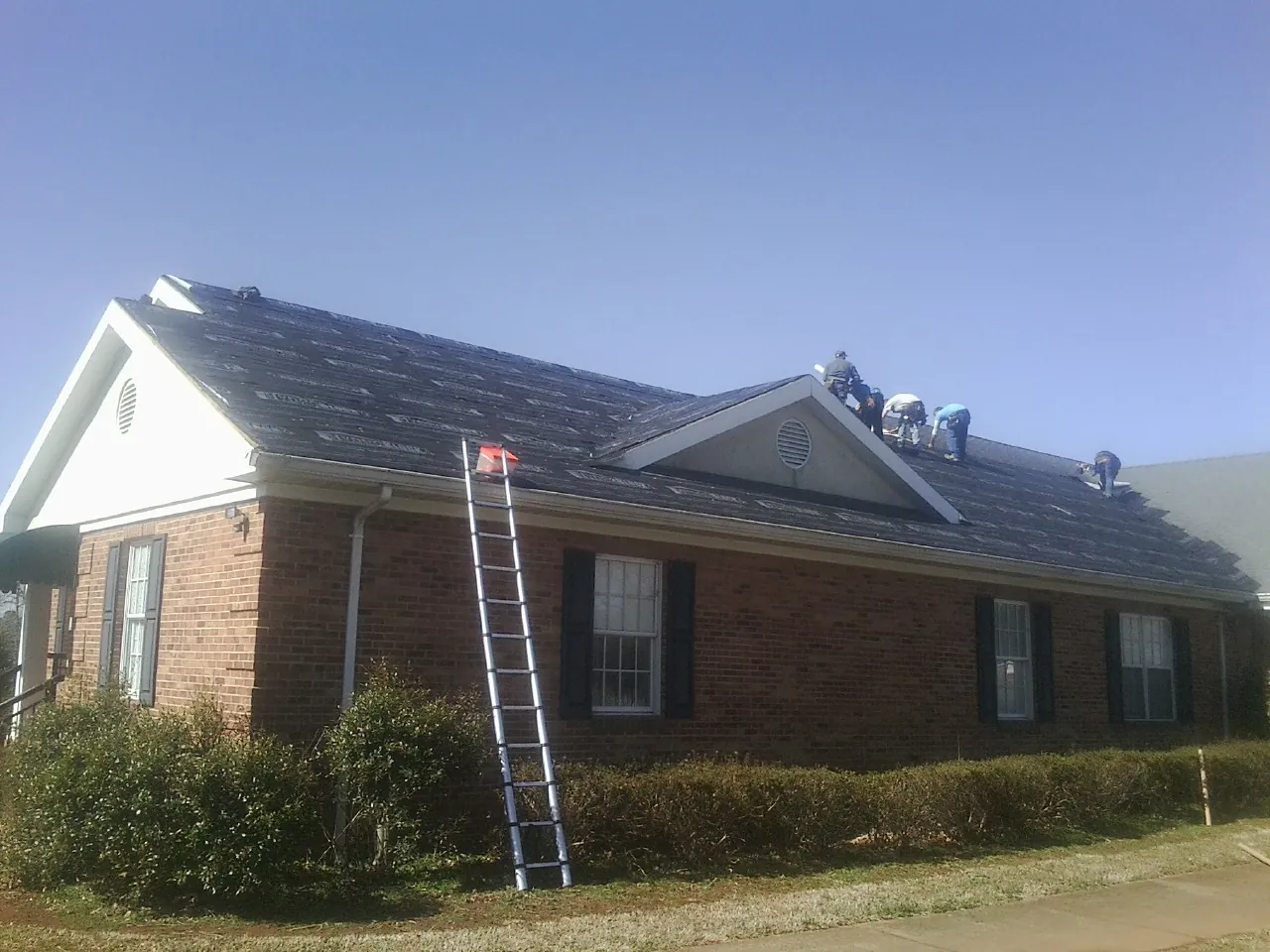 Crew tearing shingles off a brick ranch roof with a ladder set — Emergency Roof Repair work by our crew in Ocklawaha