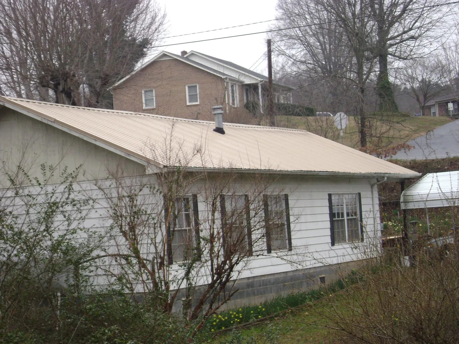 Tan metal roof on a white sided house set into a hillside — Commercial Roofing by Roofing Brothers in Ocklawaha