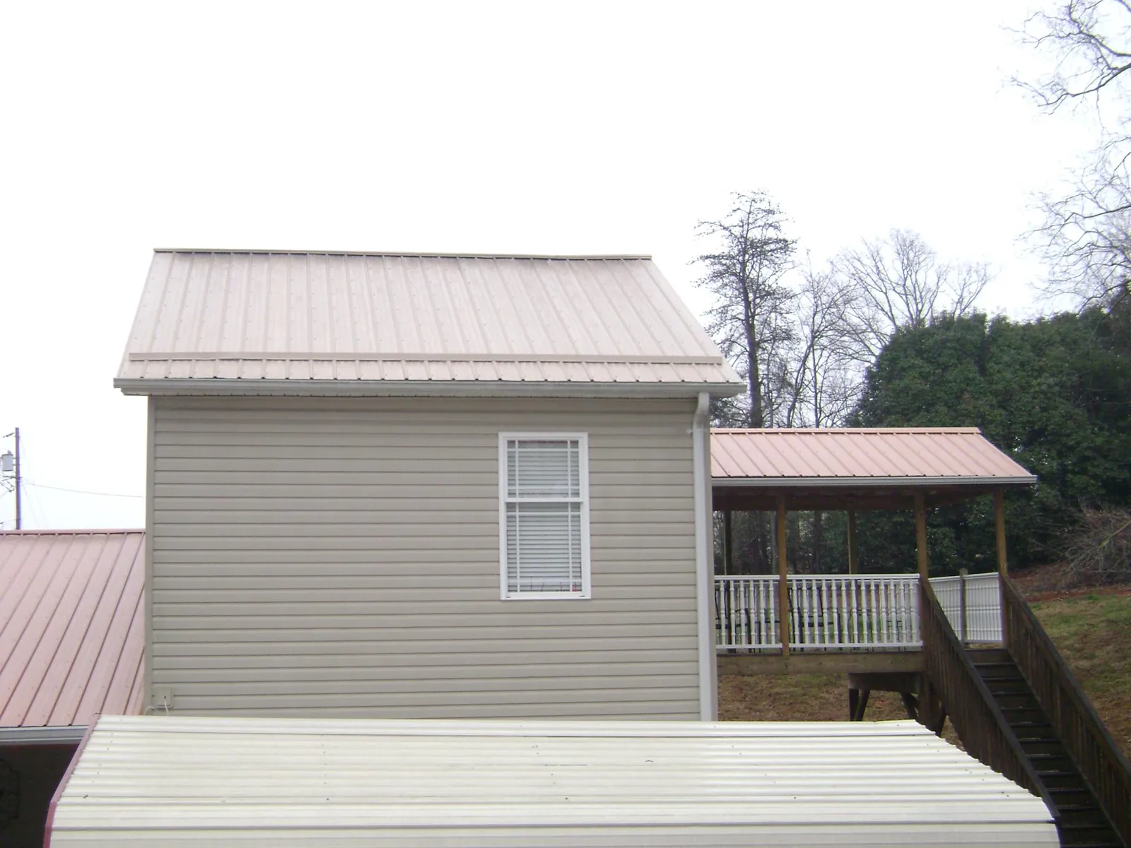 Tan metal roofs on a two story addition and attached porch, from a Roof Replacement job in Ocklawaha